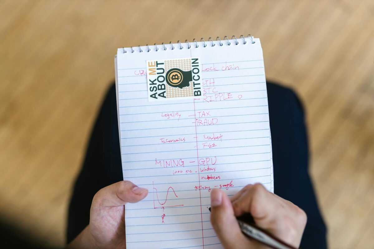 Close-up of a person writing notes about bitcoin and cryptocurrency on a notepad.